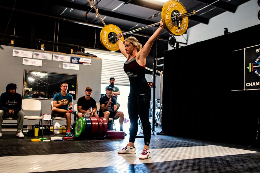 Coach Jess locking out a lift overhead at a weightlifting competition